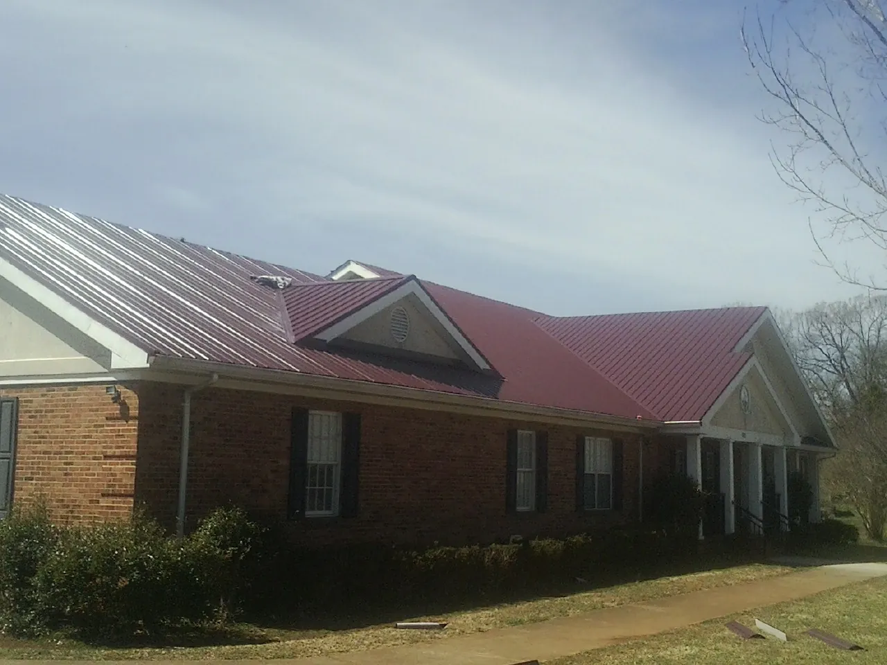 Red metal roof with gabled entries on a long brick building, from a Hail Damage Roof Repair job in Fellsmere