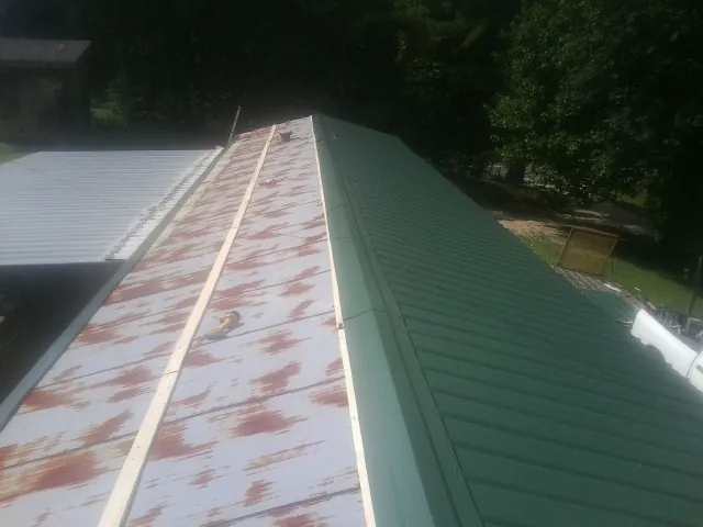 Old rusted panels beside newly installed green metal roofing — Wind Damage Roof Repair by Roofing Brothers in Fellsmere