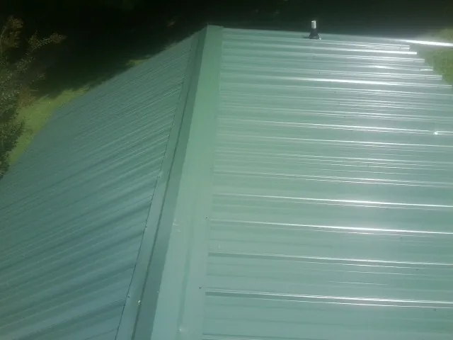New green metal panels meeting at the ridge of a roof — Flat Roof Repair work by our crew in Fellsmere