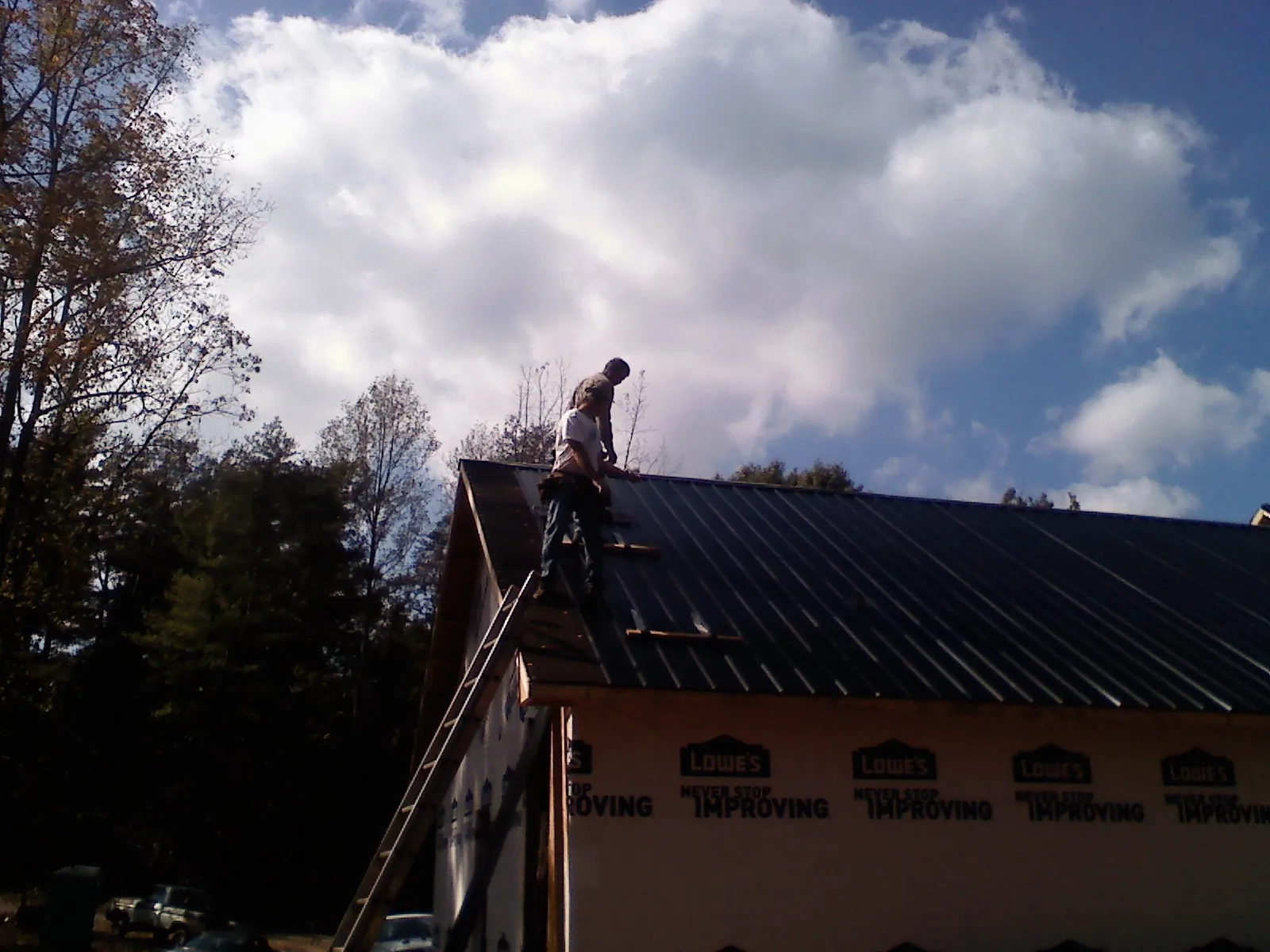 Roofer fastening dark metal panels high against a cloudy sky, from a Roof Inspection job in Fellsmere