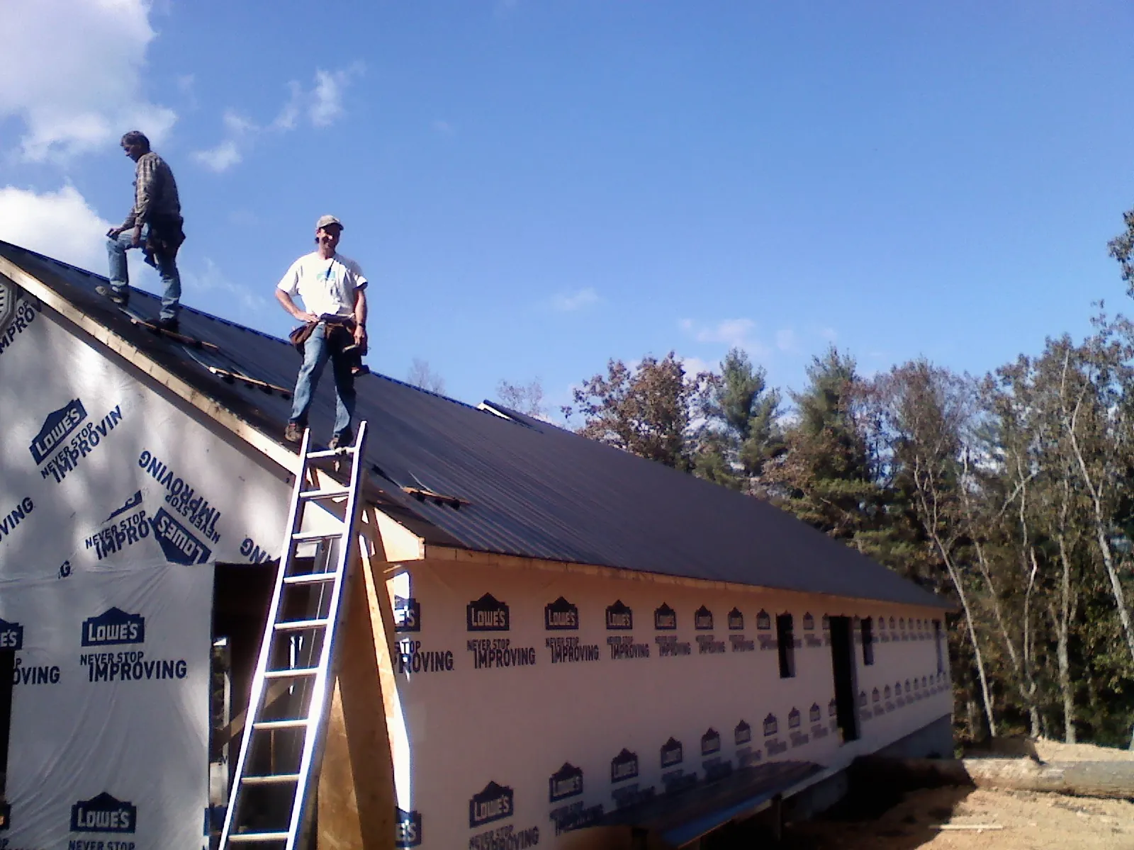 Two roofers standing on a long dark metal roof over a wrapped building in Fellsmere