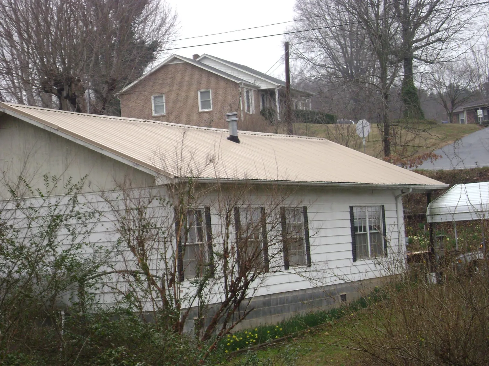 Tan metal roof on a white sided house set into a hillside — Commercial Roofing by Roofing Brothers in Fellsmere